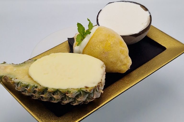 div. Eissorbets Anrichtung mit Ananas, Zitronen, Kokokusnuss, gefülltem Dessert und einer Schüssel Sahne.
