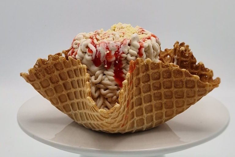Spaghetti Eisbecher Waffelschale gefüllt mit Eis, dekoriert mit Sahne und roter Fruchtsoße.